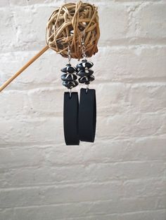 two black earrings hanging from a hook on a white brick wall next to a plant