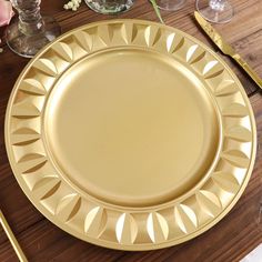 a gold plate sitting on top of a wooden table next to glasses and utensils