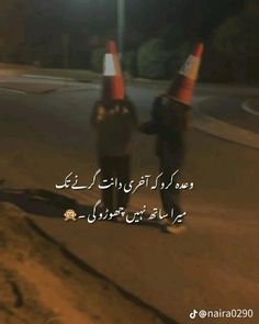 two people walking down the street at night with traffic cones on their heads and one person holding