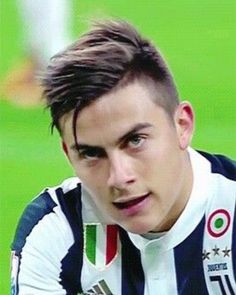 a young man sitting on top of a soccer field wearing a striped shirt and looking at the camera