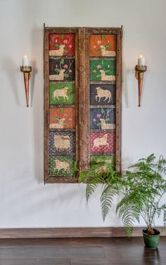 an old wooden window hanging on the wall next to a potted plant and two candles