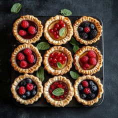 small pies with fresh berries and mint leaves on a black tray, ready to be eaten