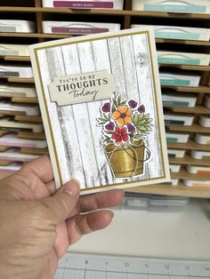 a hand holding up a card with flowers on it in front of a shelf full of books