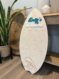 a surfboard sign sitting on top of a wooden table next to a potted plant