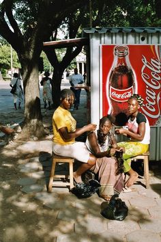 three women sitting in front of a coca cola sign