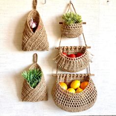 three baskets are hanging on the wall with vegetables and fruit in them, one is made out of jute