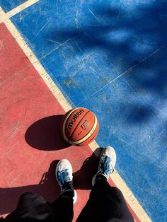 a person standing next to a basketball on top of a red and blue court with their feet in the air