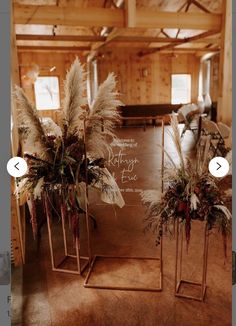 two tall vases filled with flowers and feathers on top of a wooden floor next to a chalkboard