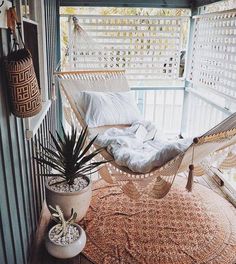 a hammock is sitting on the porch with pillows and plants next to it