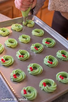 someone decorating cupcakes with green icing on a baking sheet in the kitchen