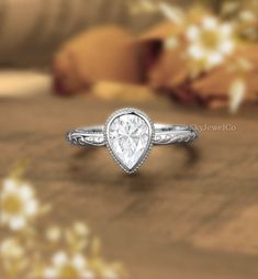 a ring with a pear shaped diamond in the center on a wooden table next to flowers