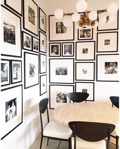 a dining room table and chairs in front of a wall full of black and white pictures