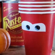 two red cups with eyes are sitting on a table next to some orange pumpkins