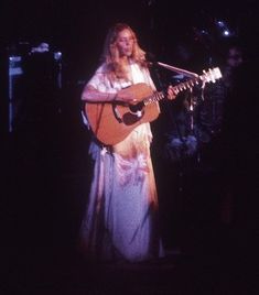 a woman holding a guitar while standing in front of a microphone