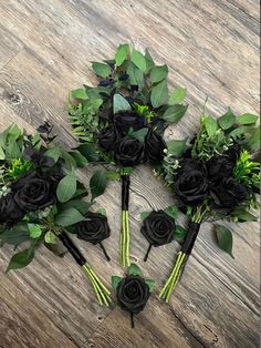 black roses and greenery are arranged on a wooden floor with green leaves in the center