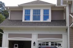 a car parked in front of a house with two garage doors and windows on each side