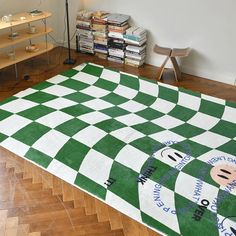 a green and white checkered area rug in a room with wooden flooring, bookshelves and shelves