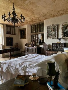 a bed sitting in a bedroom under a chandelier next to a table with two lamps on it