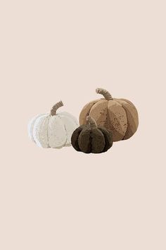 three different colored pumpkins sitting next to each other on a beige background, one is white and the other is brown