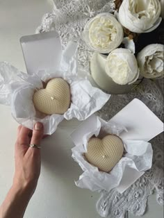 two heart shaped soaps in white paper on a lace tablecloth next to flowers