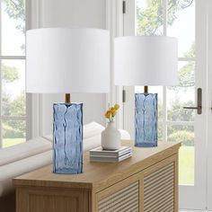 two blue vases with flowers sit on a side table in front of a window