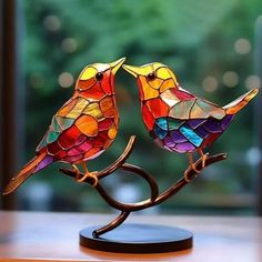 two stained glass birds sitting on top of a wooden table