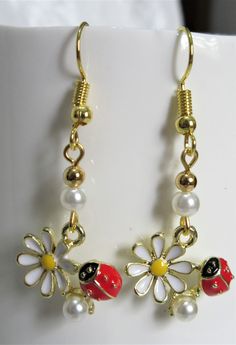 "A little red ladybug perches on a white daisy to make these 1\" earrings so adorable. The little ladybug is about 1/4\" long while the daisy is 1/2\" in diameter. Two little pearls are used as accents. These earrings are entirely gold plated. They will be slipped into an organza bag and shipped in a bubble mailer." Gold Daisy Earrings With Flower Charm, Gold Daisy Flower Earrings As Gift, Cute Red Flower Jewelry, Cute Daisy Shaped Jewelry With Flower Charm, Cute Daisy-shaped Jewelry With Flower Charm, Handmade Gold Daisy Earrings, Irish Cross, Enamel Painting, Daisy Earrings