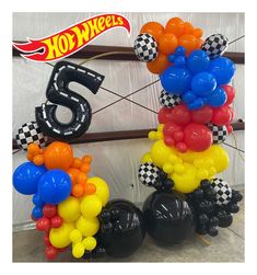 balloons are stacked on top of each other to spell out the number six in front of a hot wheels sign