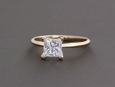 a white gold ring with a princess cut diamond set in the shants, on a grey background