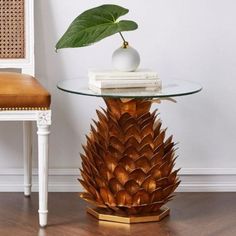 a pineapple shaped table with a glass top and gold trim around the base, next to a white chair