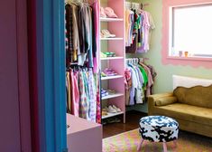 a room with a couch, chair and closet full of children's clothing on hangers