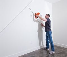 a man is using a power drill to fix a wall in an empty room with white walls