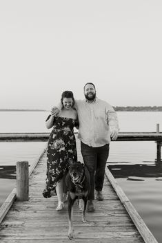 a man and woman standing on a dock with a dog