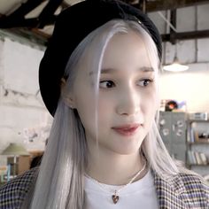 a woman with long white hair wearing a black hat and plaid shirt is looking at the camera