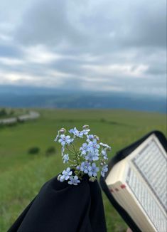 a person holding an open book in their hand with flowers growing out of the pages