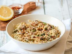 a white bowl filled with pasta and vegetables on top of a wooden cutting board next to a lemon slice