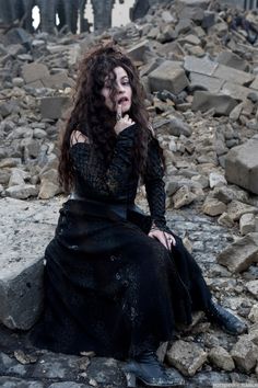 a woman sitting on top of a pile of rocks wearing a black dress and holding her hand to her mouth