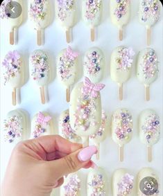 a person holding a pink nail in front of a white wall with flowers on it