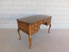 an old wooden desk with two drawers in front of a white brick wall and floor