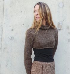 a woman standing in front of a concrete wall wearing a brown sweater and skirt with high waist