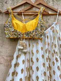 A three-piece ivory gold ruffle lehenga set with yellow mirror blouse from the Priti Sahni collection. This beautiful ivory butti georgette lehenga with big ruffle and gold gota border detailing is paired with a yellow blouse in raw silk fabric with mirror, pearl and beads hand work embroidery. The lehenga has side hanging tassels to the waistline. And the blouse has a sequins-pearl tassel tie-up at the back. The outfit is completed with an ivory sequined gold butti work dupatta with scalloped e Gold Lehenga With Mirror Work In Georgette, Yellow Pre-draped Saree With Gota Work For Party, Yellow Pre-draped Saree With Mirror Work For Reception, Elegant Yellow Lehenga With Mirror Work, Yellow Georgette Sharara With Mirror Work, Yellow Choli With Gota Work For Party, Yellow Pre-draped Saree With Mirror Work For Wedding, Yellow Georgette Unstitched Choli Blouse, Yellow Choli With Mirror Work For Party