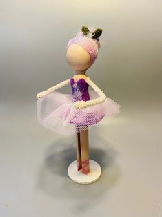 a doll is dressed in a pink and white tutu skirt, holding a purple ballerina