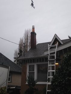 an airplane flying over a house with a ladder in the foreground and trees on the other side