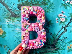 a person holding up a pink letter decorated with buttons and other things in front of a blue wall