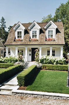 a white house with lots of flowers in the front yard and bushes on either side