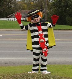 a clown dressed in black and white striped clothing standing on the side of the road