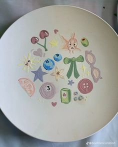 a white plate with various items drawn on the front and back of it in pastel colors