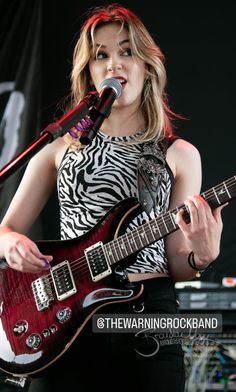 a woman holding a guitar and singing into a microphone