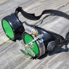 Steampunk Goggles from the fractured mind of H.G. Brasswell. Our goggles are perfect for Gifts, Cosplay, Halloween costume, or eye protection from sandstorms. If you need eye protection, we've got you covered. I present to you, a wonderful pair of black steampunk optic-conductor goggles with green lenses, silver accents and a pair of magnifying loupes (3.3x and 5x) and a SOLID BLACK elastic headstrap. This fantastical pair of goggles is perfect for any airship captain, mad scientist, wasteland w Airship Captain, Aviator Goggles, Steampunk Goggles, Time Traveler, Scarlett Witch, Steampunk Accessories