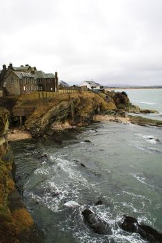 an old house sitting on top of a cliff next to the ocean with waves crashing in front of it